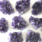 A photo of several dark purple amethyst clusters arranged on a white background. The amethyst clusters are a rich, deep purple colour. The white background provides contrast to the dark purple color of the amethyst and allows the intricate details of each cluster to be easily appreciated.