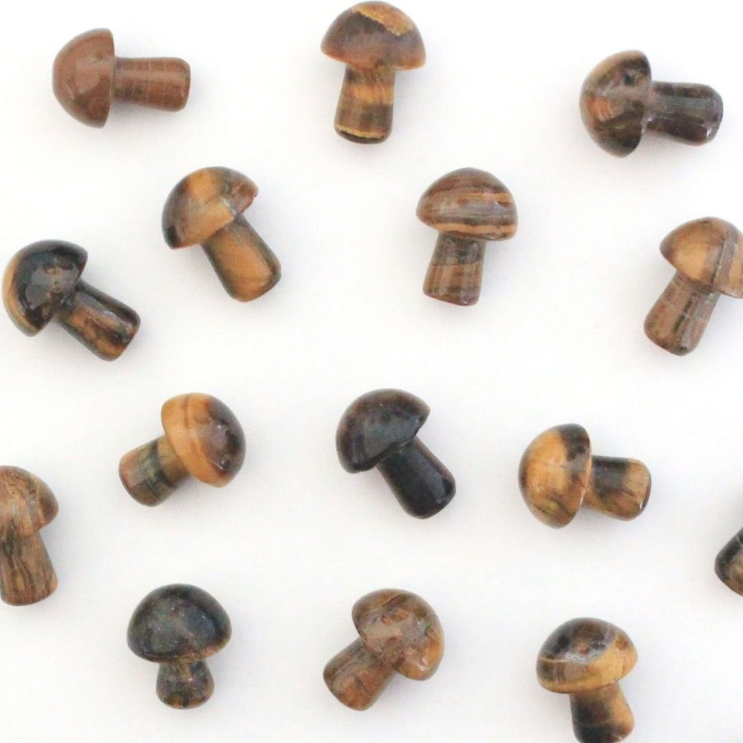 A photo of small crystal mushrooms made from tiger's eye, a type of quartz mineral with a distinctive golden-brown colour and chatoyancy, or a reflective quality that gives it a shimmering appearance. Each mushroom has a rounded cap and a short stem, and has been polished to a smooth and shiny finish