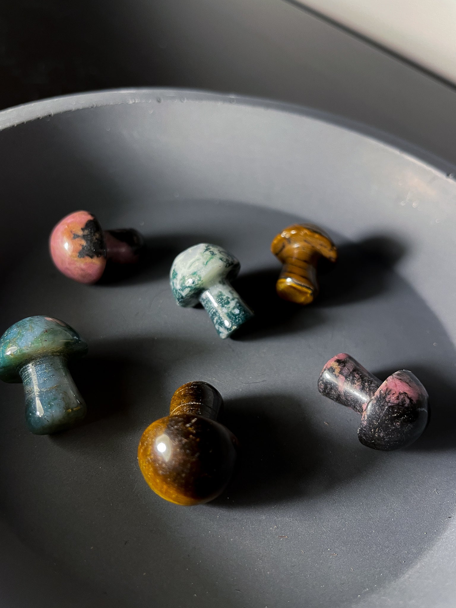 A photo of a group of miniature crystal mushrooms, each made from a different type of crystal or mineral. Each mushroom has a rounded cap and a short stem, and has been polished to a smooth and shiny finish. 
