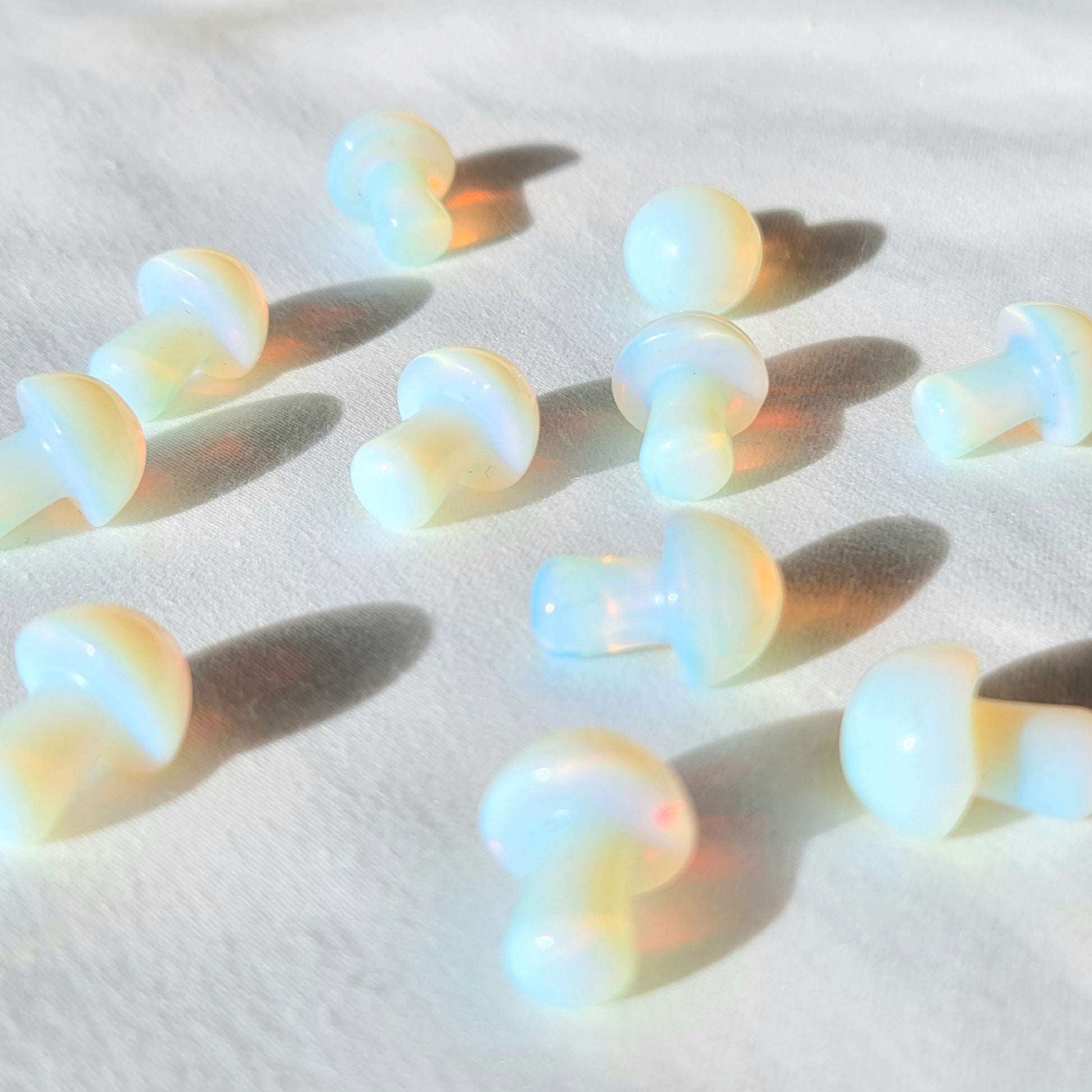 A photo of small crystal mushrooms made from opalite, a type of glass that resembles the iridescent play of colours found in natural opals. Each mushroom has a rounded cap and a short stem, and has been polished to a smooth and shiny finish. 
