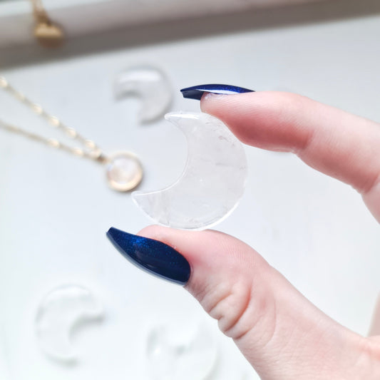 A photo of a moon carving made from clear quartz, a transparent variety of quartz mineral that is known for its clarity and reflective properties. The surface of the moon is polished to a smooth, shiny finish, with natural variations in texture and colour visible in the stone.