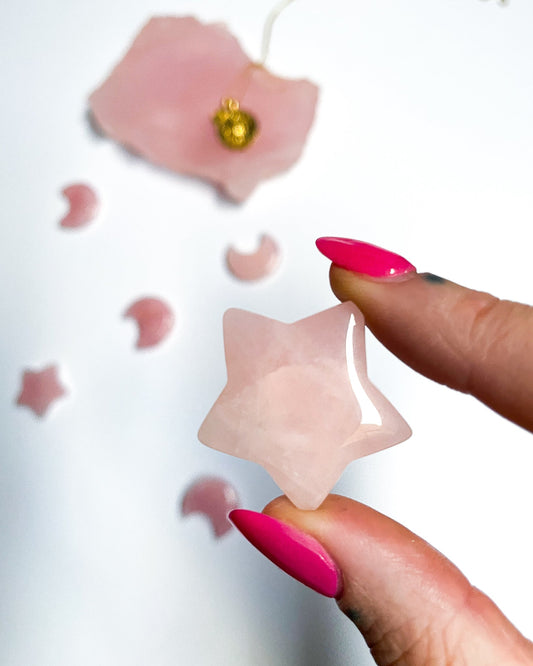 A photo of a small rose quartz carving in the shape of a star. The rose quartz is a pale, translucent pink color and has been carved and polished to a smooth, shiny finish. 